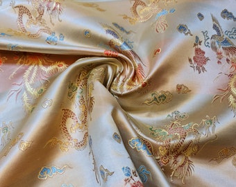 Könnte beinhalten: Nahaufnahme eines goldenen Stoffes mit einem aufwendigen Stickmuster aus Drachen und Wolken. Der Stoff hat einen dezenten Glanz und eine weiche Textur.