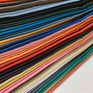 May include: A stack of fabric swatches in a variety of colours, including red, orange, yellow, green, blue, and purple. The fabric is folded neatly and arranged in a rainbow pattern.
