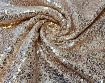 May include: Close-up of a gold sequined fabric. The sequins are arranged in a swirling pattern, creating a shimmering effect.