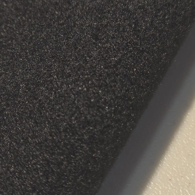K&ouml;nnte beinhalten: Nahaufnahme eines dunkelgrauen, strukturierten Stoffes. Das Material scheint weich und leicht flauschig zu sein, mit einem dezenten Glanz. Der Stoff ist gefaltet und gibt einen Einblick in eine hellere Oberfl&auml;che.