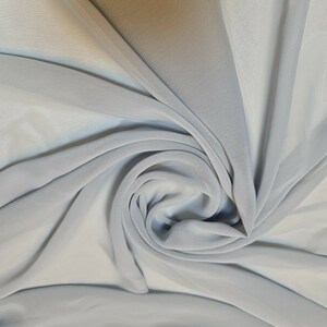 May include: A close-up of a light blue fabric with a soft, flowing texture. The fabric is draped and folded, creating a swirling pattern.