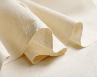 May include: Close-up of a folded, off-white fabric. The fabric is soft and appears to be cotton or a similar natural fiber. The folds create shadows and texture, highlighting the material's drape and thickness. The overall tone is neutral and natural.