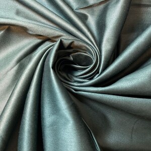 May include: Close-up of a dark green satin fabric with a smooth, silky texture. The fabric is draped and folded, creating a swirling pattern.