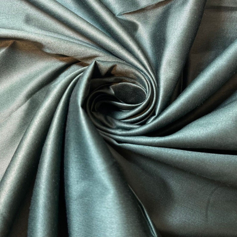 May include: Close-up of a dark green satin fabric with a smooth, silky texture. The fabric is draped and folded, creating a swirling pattern.