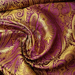 Op de afbeelding: Paarse stof met een gouden paisley-patroon. De stof is textuurrijk en voelt luxueus aan.