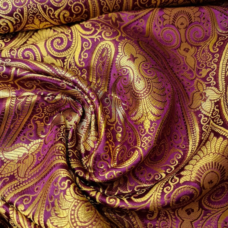 Op de afbeelding: Paarse stof met een gouden paisley-patroon. De stof is textuurrijk en voelt luxueus aan.