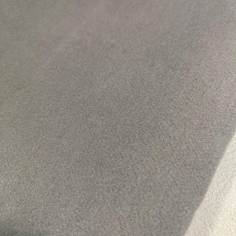 K&ouml;nnte beinhalten: Nahaufnahme eines grauen Stoffes mit einer weichen, strukturierten Oberfl&auml;che. Der Stoff scheint eine einfarbige Farbe zu haben, mit subtilen Farbtonvariationen. Das Material wird wahrscheinlich f&uuml;r Kleidung oder Heimdekoration verwendet.