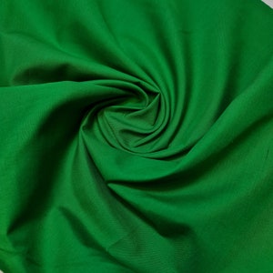 Pode incluir: Um close-up de um tecido verde liso com uma textura suave e fluida. O tecido está dobrado e drapeado, criando um padrão de redemoinho.
