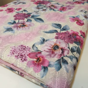 May include: Pink floral lace fabric with a white background. The fabric has a delicate floral pattern with pink, white, and blue flowers.