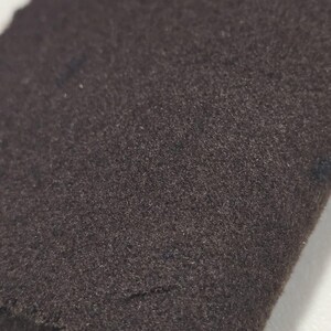K&ouml;nnte beinhalten: Nahaufnahme eines dunkelbraunen Stoffes mit einer weichen, strukturierten Oberfl&auml;che. Der Stoff scheint eine einfarbige Farbe zu haben, mit subtilen Farbtonvariationen. Das Material ist wahrscheinlich ein Textil, m&ouml;glicherweise Wolle oder eine &auml;hnliche Faser.
