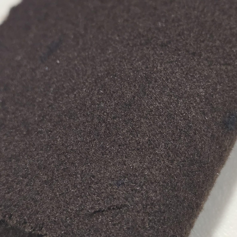 K&ouml;nnte beinhalten: Nahaufnahme eines dunkelbraunen Stoffes mit einer weichen, strukturierten Oberfl&auml;che. Der Stoff scheint eine einfarbige Farbe zu haben, mit subtilen Farbtonvariationen. Das Material ist wahrscheinlich ein Textil, m&ouml;glicherweise Wolle oder eine &auml;hnliche Faser.