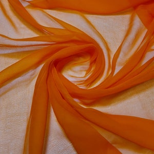 May include: A close-up of a bright orange sheer fabric, draped and folded to create a swirling pattern. The fabric is lightweight and translucent, with a soft, flowing texture.