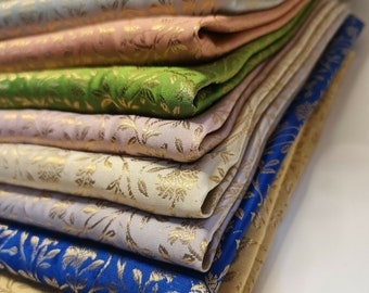 May include: A stack of fabric swatches in various colors and patterns, including gold, green, blue, pink, and white. The fabric has a subtle floral design.