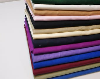 May include: A stack of folded fabric in various colors, including green, white, tan, pink, black, and blue. The fabrics appear to be cotton or a similar material, with a smooth texture. The stack is neatly arranged, showcasing the different hues.