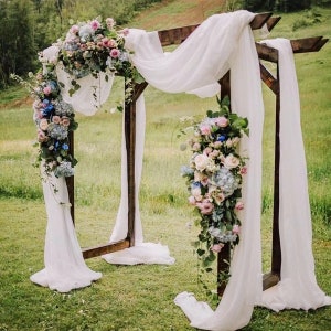 May include: A wooden wedding arch decorated with white fabric and cascading bouquets of pink, blue, and white flowers.