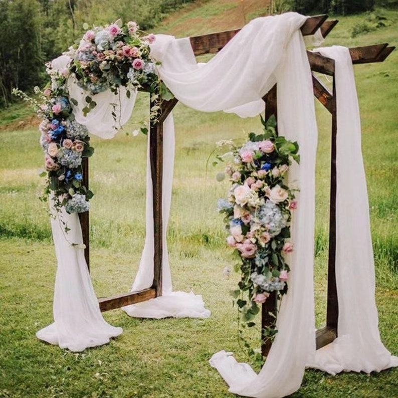 May include: A wooden wedding arch decorated with white fabric and cascading bouquets of pink, blue, and white flowers.