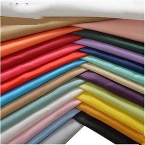 May include: A stack of fabric swatches in various colours, including white, beige, light blue, pink, yellow, orange, red, and green. The fabric is smooth and appears to be satin.