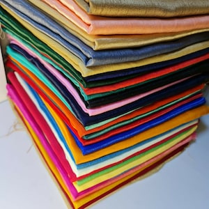 Può includere: Un mucchio di campioni di tessuto colorati in varie tonalità di blu, verde, rosso, arancione, giallo, rosa e viola. Il tessuto è liscio e setoso.