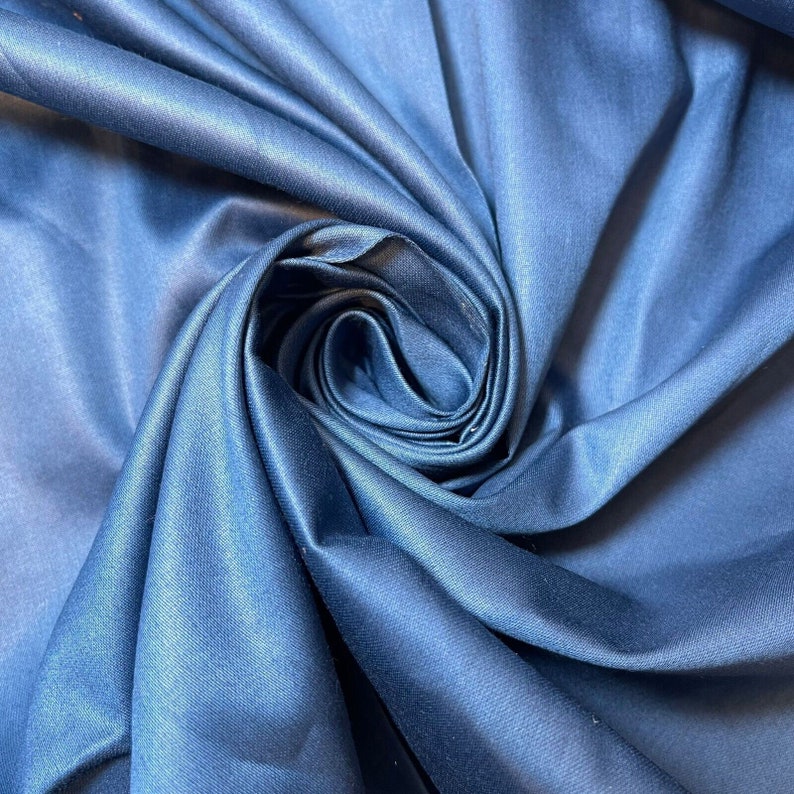 May include: A close-up of a blue fabric with a smooth, silky texture. The fabric is folded and draped in a way that creates a swirling pattern.