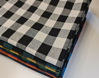May include: A stack of folded checkered fabric napkins in various colors. The top napkin is black and white, followed by green, yellow, orange, and blue. The napkins have a classic gingham pattern.