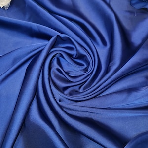 May include: A close-up of a smooth, royal blue fabric with a soft, silky texture. The fabric is draped and folded, creating a swirling pattern.