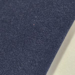 K&ouml;nnte beinhalten: Nahaufnahme eines marineblauen Stoffes mit strukturierter Oberfl&auml;che. Der Stoff scheint gefaltet zu sein und gibt einen Blick auf eine wei&szlig;e Oberfl&auml;che darunter frei. Die Textur des Stoffes ist sichtbar.