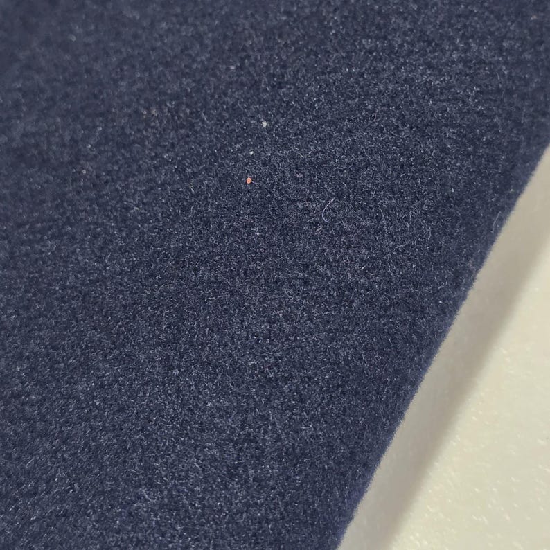 K&ouml;nnte beinhalten: Nahaufnahme eines marineblauen Stoffes mit strukturierter Oberfl&auml;che. Der Stoff scheint gefaltet zu sein und gibt einen Blick auf eine wei&szlig;e Oberfl&auml;che darunter frei. Die Textur des Stoffes ist sichtbar.