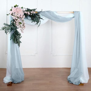May include: A wedding arch decorated with light blue sheer fabric and a cascading garland of pink flowers and green leaves.