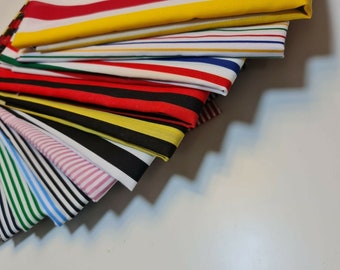 May include: A stack of striped fabric in various colors, including red, yellow, blue, black, and white. The fabric is folded in a fan shape, with the top layer being a red, yellow, and blue striped fabric.