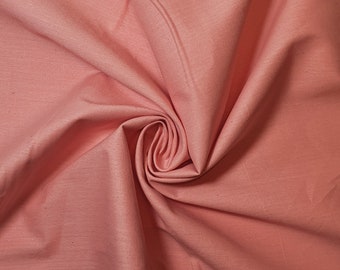 Peut inclure: Gros plan sur un tissu doux de couleur pêche à la texture lisse. Le tissu est plié et drapé, créant un effet doux et fluide.