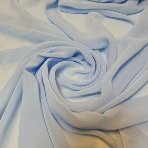 Può includere: Un tessuto leggero di colore azzurro chiaro, piegato e drappeggiato in un motivo morbido e fluido. Il tessuto è liscio e delicato, con un leggero bagliore.
