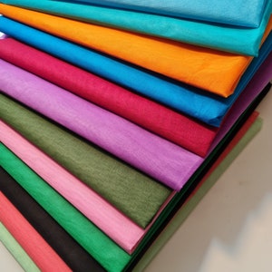 Puede incluir: Una pila de hojas de tela de colores en varios tonos de azul, verde, rosa, morado, naranja y rojo. La tela es lisa y parece estar hecha de un material ligero.