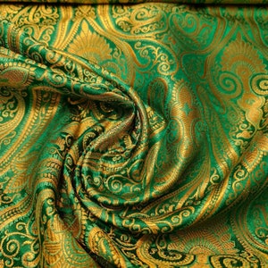 Op de afbeelding: Groene en gouden stof met een paisley-patroon. De stof is gevouwen en gedrapeerd, waardoor de textuur en de details van het ontwerp zichtbaar worden.