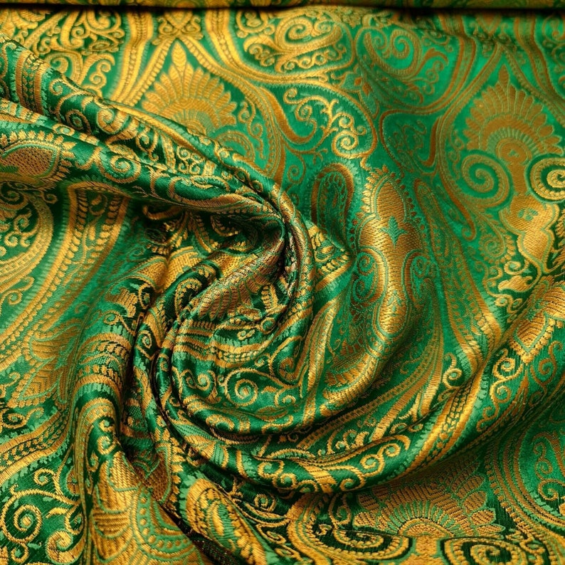 Op de afbeelding: Groene en gouden stof met een paisley-patroon. De stof is gevouwen en gedrapeerd, waardoor de textuur en de details van het ontwerp zichtbaar worden.