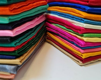May include: A stack of colorful fabric swatches in various shades of green, red, blue, yellow, pink, and white. The fabric is arranged in a neat pile, showcasing the different colors and textures.