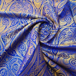 Op de afbeelding: Blauw en gouden paisley stof met een draaiend patroon. De stof is zacht en luxueus, perfect voor bekleding of kleding.
