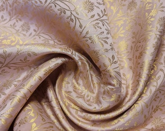 Op de afbeelding: Een close-up van een roze stof met een gouden bloemenpatroon. De stof is zacht en heeft een subtiele glans.