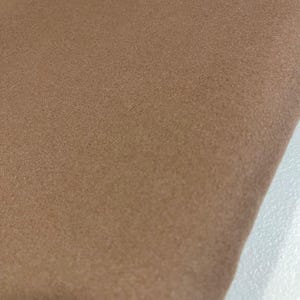 K&ouml;nnte beinhalten: Nahaufnahme eines St&uuml;cks beigen Stoffes. Der Stoff hat ein weiches, strukturiertes Aussehen. Die Farbe ist ein warmer, neutraler Ton, und das Material scheint gefaltet zu sein. Der Hintergrund ist hell.