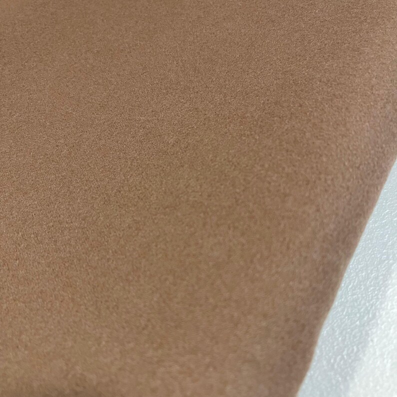 K&ouml;nnte beinhalten: Nahaufnahme eines St&uuml;cks beigen Stoffes. Der Stoff hat ein weiches, strukturiertes Aussehen. Die Farbe ist ein warmer, neutraler Ton, und das Material scheint gefaltet zu sein. Der Hintergrund ist hell.