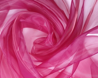 May include: A close-up of a pink sheer fabric with a gradient from a darker pink to a lighter pink. The fabric is draped and folded, creating a soft and flowing texture.