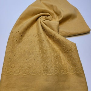 May include: A mustard yellow fabric with a delicate embroidered pattern. The fabric has a scalloped edge and small holes throughout the design.