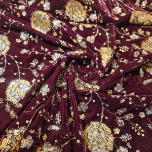 K&ouml;nnte beinhalten: Burgunderfarbener Samtstoff mit goldenen und silbernen Pailletten in einem Blumenmuster.