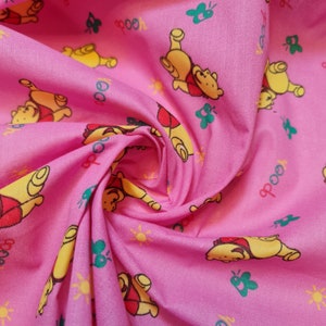 May include: Pink fabric with a repeating pattern of cartoon bears, butterflies, suns, and the word "Pooh".