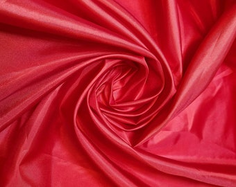 May include: Close-up of a smooth, red fabric with a swirling, rose-like pattern. The fabric is soft and silky, with a subtle sheen.