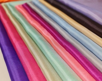 May include: A collection of fabric swatches in various colors, including purple, pink, green, and blue. The fabric is smooth and silky, with a slight sheen.