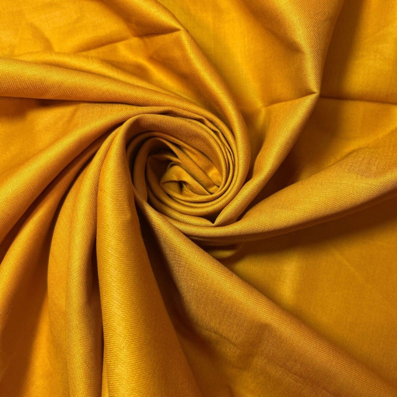 May include: A close-up of a smooth, golden yellow fabric. The fabric is folded and draped to create a soft, flowing effect.