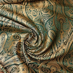 Op de afbeelding: Groene en gouden brokaat stof met een paisley patroon. De stof is gevouwen en gedrapeerd, waardoor de textuur en de details van het ontwerp zichtbaar worden.