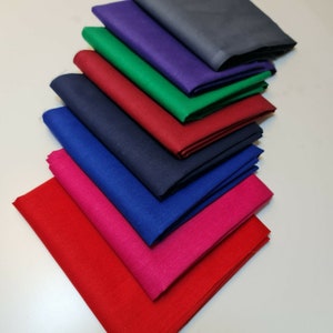 Può includere: Un mucchio di otto quadrati di tessuto di diversi colori, tra cui rosso, blu, verde, viola e blu navy. I quadrati di tessuto sono piegati a metà e impilati uno sopra l'altro.