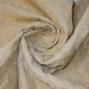 Puede incluir: Primer plano de una tela beige con un delicado patrón de hojas bordadas. La tela es suave y texturizada, con un brillo sutil.