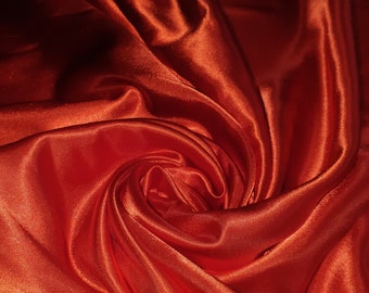 May include: A close-up of a deep red satin fabric, with soft, flowing folds and a luxurious sheen.